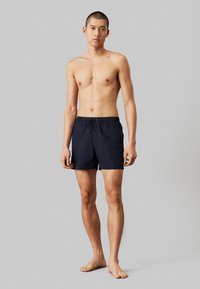 Shorts de bain bleu marine avec taille à cordon de serrage, fabriqués en tissu léger, dotés d'un design minimaliste et d'un petit logo sur le côté.