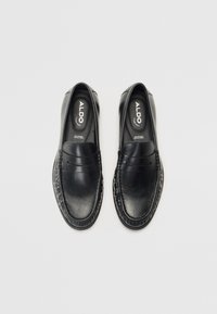 Sorte skinnloafers med en glatt overflate og sydd detaljer. Har en hevet rem over toppen og polstrede innersåler.
