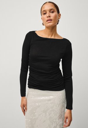 Zwarte lange mouw top met een off-shoulder halslijn en geplooide textuur. Combinatie met een glanzende paillettenrok.