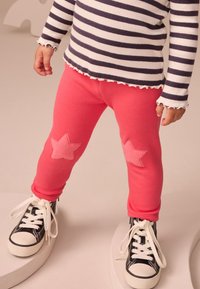 Pink sweatpants with star appliqués on the knees, paired with black high-top sneakers, and a navy and white striped long-sleeve top.