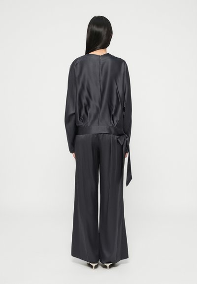 Ținută din satin negru, cu un top lejer care are un detaliu cu fundă în talie și pantaloni evazați. Textură netedă, design minimalist.