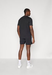 Camiseta negra y pantalones cortos a juego, ambos hechos de tela suave. Llevados con zapatillas blancas y calcetines hasta el tobillo, vistos desde la parte de atrás.