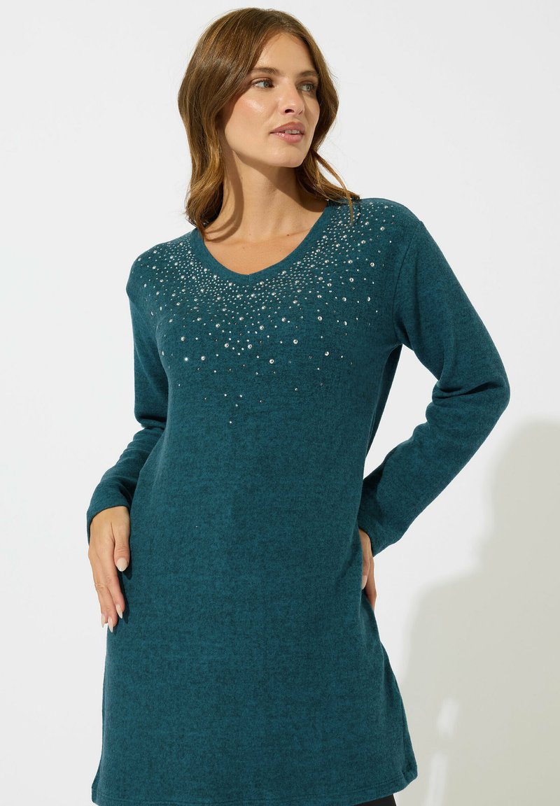 Vestito maglione verde acqua con maniche lunghe, scollo a V e paillettes decorative sul petto. Tessuto morbido, lunghezza al ginocchio e taglio rilassato.
