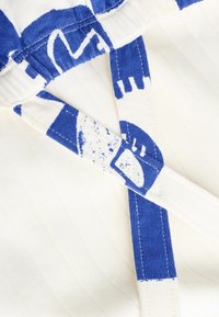 Blau-weißer Stoff mit Muster und Streifen, der eine gewebte Textur und kontrastierende Träger aufweist. Sichtbare Nähte verleihen Details.