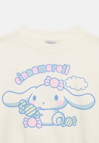 Cartoon character Cinnamoroll with long ears holding pastel-colored candies, pink cheeks, and a cloud, printed on a white shirt.