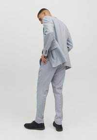 Lichtblauw maatpak met een enkelvoudige blazer en slim-fit broek. Gestructureerde stof en zwarte suède schoenen.