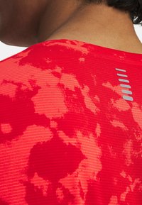 Rotes Sportshirt mit strukturierter, gemusterter Oberfläche und einem reflektierenden Akzent auf der Rückseite. Das Design hat einen subtilen Ombre-Effekt.