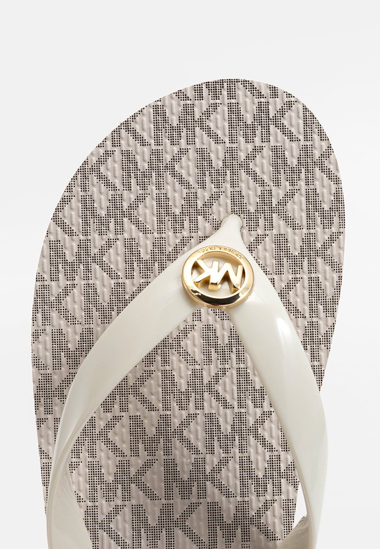 Tongs blanches avec une sangle brillante, arborant un logo circulaire doré. La semelle présente un motif texturé en gris clair avec des lettres répétées.