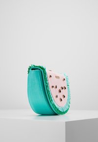 Una borsa a forma arrotondata con un esterno testurizzato turchese, un lato frontale rosa con accenti neri e dettagli frangiati verdi.