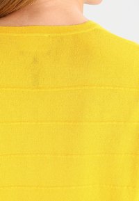 Top giallo a maglia con texture a righe orizzontali, presenta un collo rotondo e un tessuto liscio e leggero.