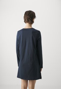 Abito navy a maniche lunghe realizzato in tessuto morbido, caratterizzato da una silhouette dritta e un collo rotondo, con una leggera spaccatura laterale per un tocco di originalità.