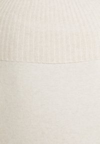 Suéter de punto beige claro con textura acanalada en la parte superior y un acabado suave en la parte inferior. Tejido suave con una transición sin interrupciones entre los patrones.