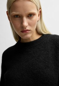 Maglione nero texture con collo rotondo, realizzato in un tessuto morbido e dalla vestibilità comoda, che punta sulla semplicità e sul calore.