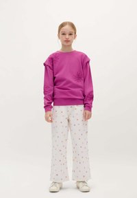 Lilla sweatshirt med blomsterbroderi, parret med hvide bukser med et multicolor blomster mønster. Modellen bærer hvide sneakers.