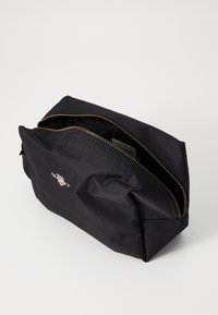 Svart nylon kosmetikkveske med teksturert overflate, to glidelåslommer og en kontrastfarget glidelås i gull. Har en liten logo på siden.