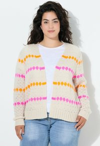 Strikket cardigan i creme med rosa og orange geometriske striber. Åbent frontdesign, ribbede manchetter og en afslappet pasform. Båret over en hvid top.