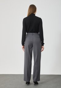 Top negru cu mâneci lungi asortat cu pantaloni gri cu talie înaltă. Pantalonii au un design drept și buzunare la spate.