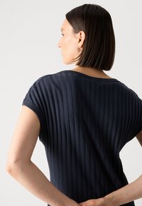 Sini ribbed toppi lyhyillä hihoilla ja rentoa istuvuutta, jossa on kaareva kaula-aukko ja pehmeä rakenne. Näkyvät saumat ja minimalistinen muotoilu.