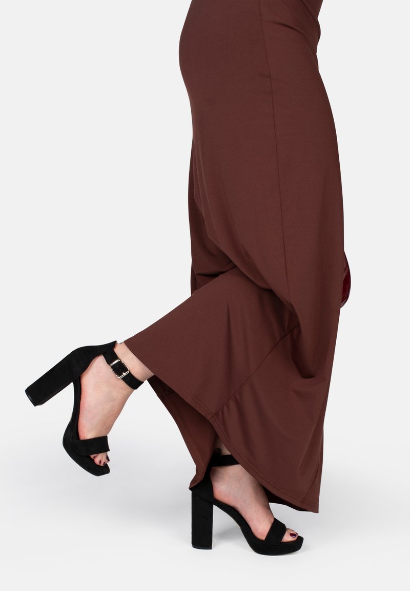 Vestido marrón con un dobladillo fluido, combinado con sandalias de tacón negro con tira al tobillo y un acabado de ante texturizado.