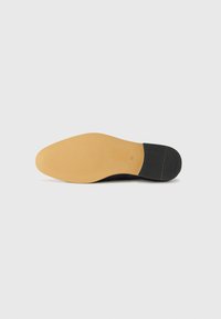 Semelle de chaussure en cuir noir avec un design texturé, dotée d'un fond en caoutchouc beige lisse et d'un petit accent de talon noir.