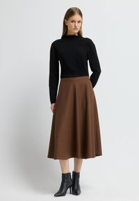 Top negro de manga larga combinado con una falda marrón hasta la rodilla con un patrón texturizado, complementado con botas negras hasta el tobillo.