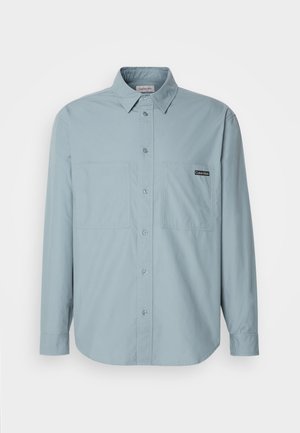 Jasnoniebieska koszula zapinana na guziki z długimi rękawami, dwoma kieszeniami na piersi, klasycznym kołnierzykiem i małą metką marki na lewej kieszeni. Wykonana z bawełny.
