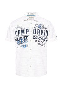 Lyhythihainen, valkoinen napillinen paita, jossa on teksturoitu kangas. Sisältää sinisiä painettuja grafiikoita ja tekstiä, mukaan lukien "CAMP DAVID" ja erilaisia kuvioita.