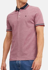 Rode en marineblauwe poloshirt met een kraaghalslijn, voorzien van drie knopen, gestreepte accenten op de mouwen en een klein logo op de borst.