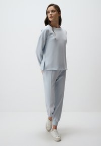Jasnoniebieska, luźno dopasowana bluza z bocznymi rozcięciami, w połączeniu z dopasowanymi dresami i białymi sportowymi butami, wykonana z miękkiego materiału.