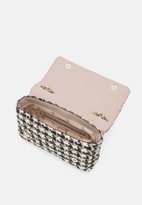 Zwart-wit houndstooth stoffen tas met beige interieur, gouden kettingbevestigingen en een ritsvak aan de binnenkant.