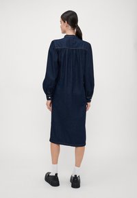 Jeans obleka v temno modri barvi z dolgimi, napihnjenimi rokavi. Ima ovratnik in nabran detajl na hrbtu. V kombinaciji s črnimi platform čevlji.