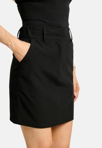 Fekete szoknya nadrág sima textúrával, rugalmas derékpánttal, oldalzsebekkel és szabott szabással a testhez simuló megjelenésért.
