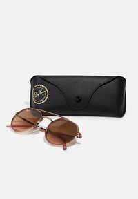 Ochelari de soare cu lentile de culoare roz deschis, �într-o formă geometrică. Cadru din metal cu accente aurii roz, însoțiți de o husă din piele neagră.