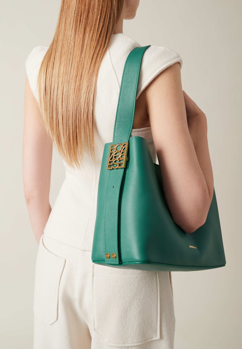 Green leather handbag with a structured shape, featuring a gold-tone hardware accent and a textured finish. Adjustable strap for carrying.