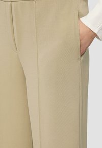 Beige Hose aus glattem Stoff, mit einer Seitentasche und einer sauberen Nahtverarbeitung, mit einem elastischen Bund für Komfort.