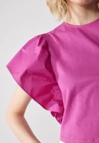 Fuchsia Kurzarmoberteil mit Rüschensäumen, hergestellt aus weichem Baumwollstoff. Glatte Textur mit einem lässigen, entspannten Schnitt.
