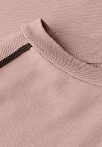 Nahaufnahme eines staubigen rosa Strickshirts mit Rippenkragen und einem dunkelbraunen Akzentdetail an der Schulter.