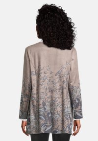 Chaqueta floral de manga larga beige con textura suave, que presenta acentos de estampado floral gris y de leopardo en el dobladillo y las mangas.