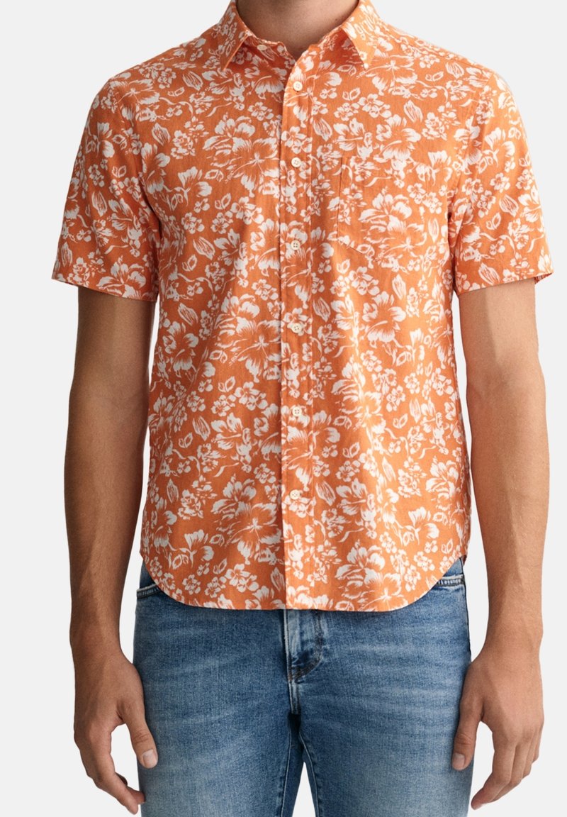 Camicia a maniche corte con bottoni di un vivace arancione con motivo floreale bianco; caratterizzata da un colletto e un orlo curvo, realizzata in tessuto traspirante.