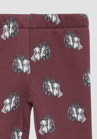 Bordowe legginsy o gładkiej fakturze z powtarzającym się wzorem głów koni w czerni i bieli. Elastyczny pas dla wygody.