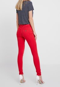Jean skinny rouge avec une texture lisse, taille haute et coutures contrastées, associé à un haut à rayures noir et blanc.