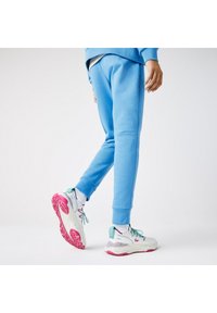Blauwe katoenen sweatpants met taps toelopende pijpen, voorzien van ribgebreide boorden. Gemaakt in combinatie met meerkleurige sportschoenen met roze zolen en textuurdetails.