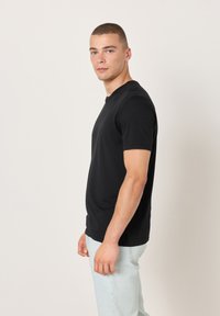 Crna pamučna majica s okruglim izrezom i kratkim rukavima, nošena s svijetlo plavim trapericama. Jednostavan dizajn bez vidljivih uzoraka ili naglasaka.