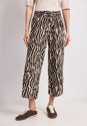 Pantalon mi-long avec motif zèbre noir et beige, taille ceinturée, porté avec des baskets marron foncé à lacets blancs.