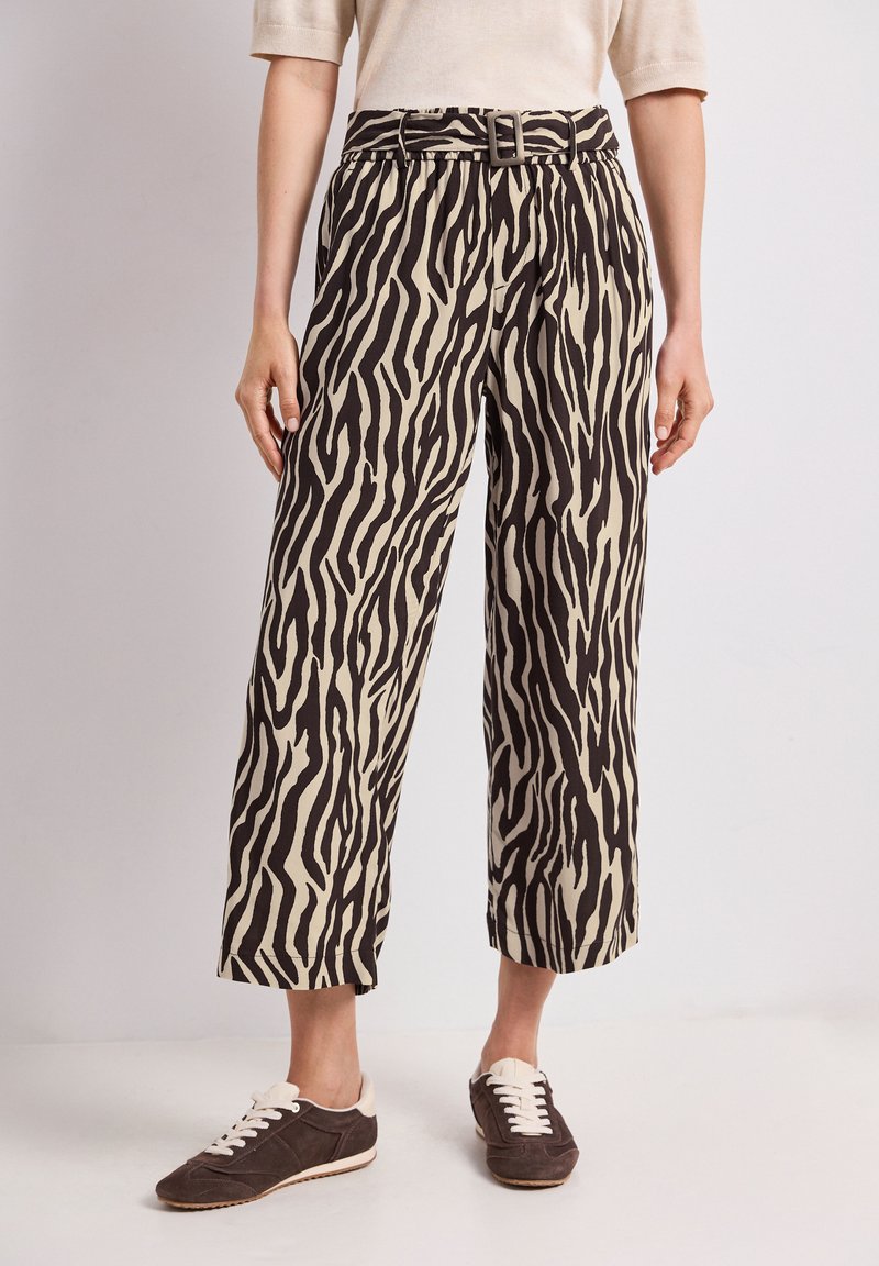Pantalon mi-long avec motif zèbre noir et beige, taille ceinturée, porté avec des baskets marron foncé à lacets blancs.
