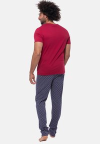 Rød kortærmet t-shirt og blå mønstrede pyjamasbukser med små hvide og lyserøde prikker, lavet af blødt, elastisk stof.