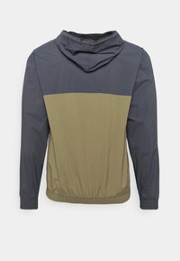 Farveblokeret jakke med en mørkeblå øverste sektion og en khaki nederste sektion. Fremstillet af letvægtsmateriale med hætte og elastiske manchetter.