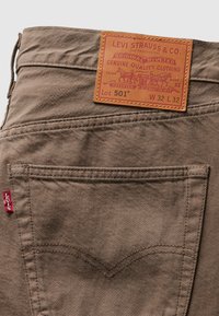 Brune denimjeans med en læderpatch mærket "Levi Strauss & Co.". Med baglommer og et rødt mærke på sidesømmen.