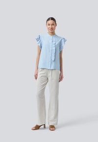 Light blue short-sleeve blouse with ruffled accents, button front, paired with white vertical striped trousers and brown open-toe heels.