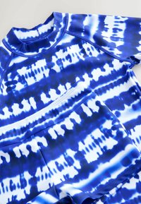 Sinine ja valge mustriga rash guard, millel on kõrge kaelus ja lühikesed varrukad, valmistatud venivast kangast, millel on sile tekstuur.